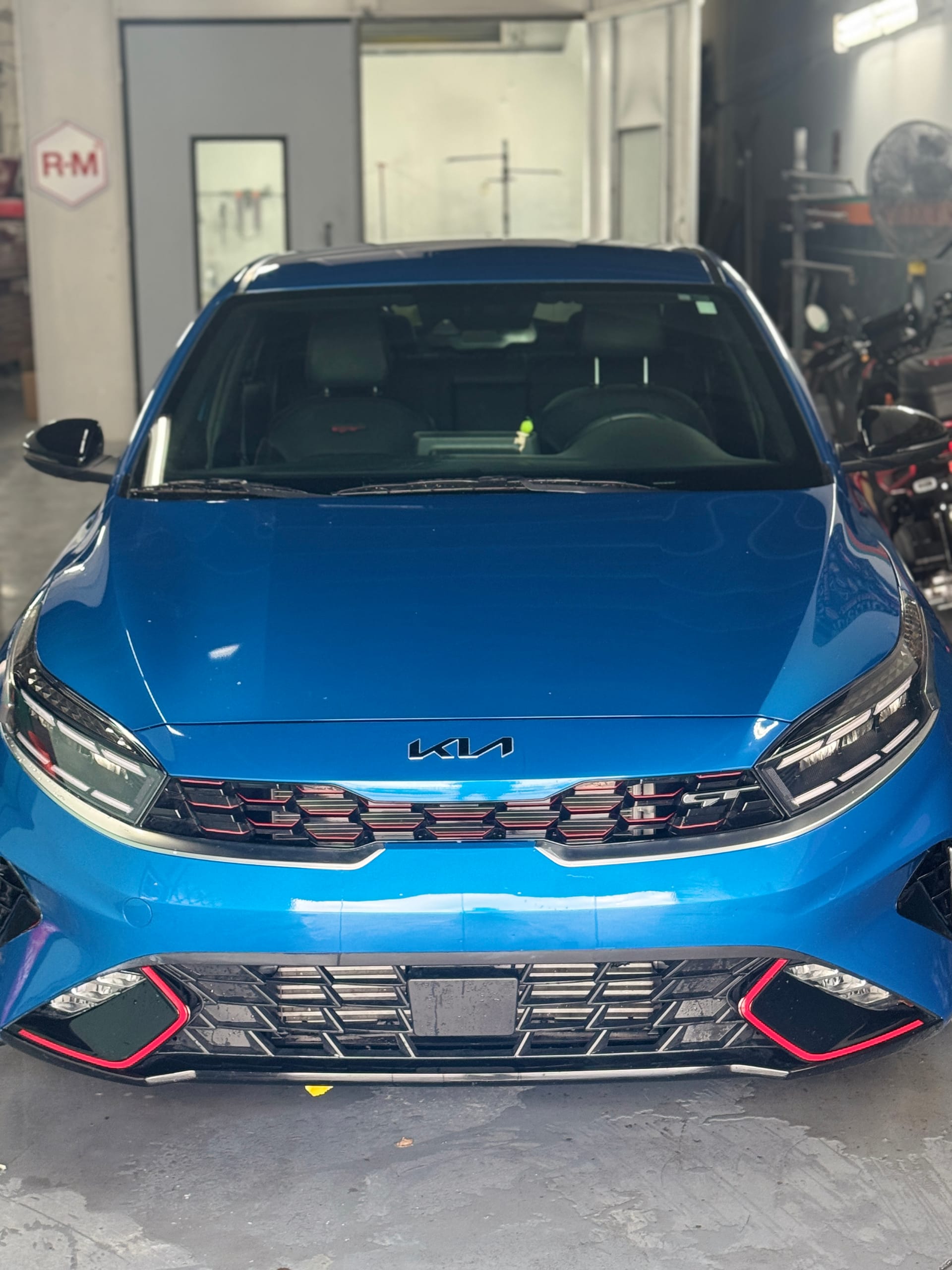 Blue Kia Forte GT with the front end repaired, straight-on view in the shop
