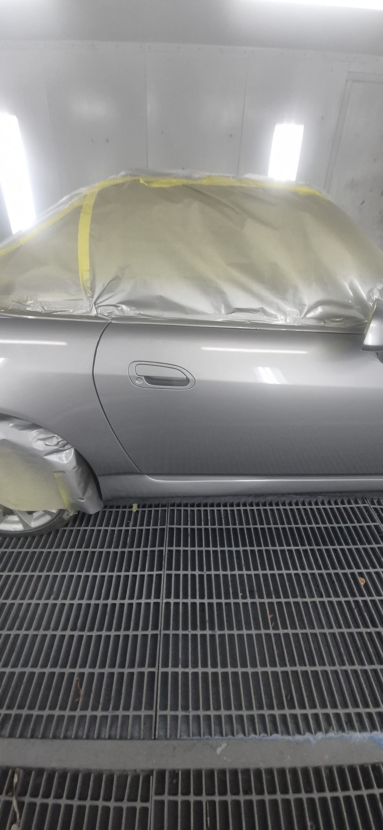 The roadster masked with paper and tape inside the paint booth, side view