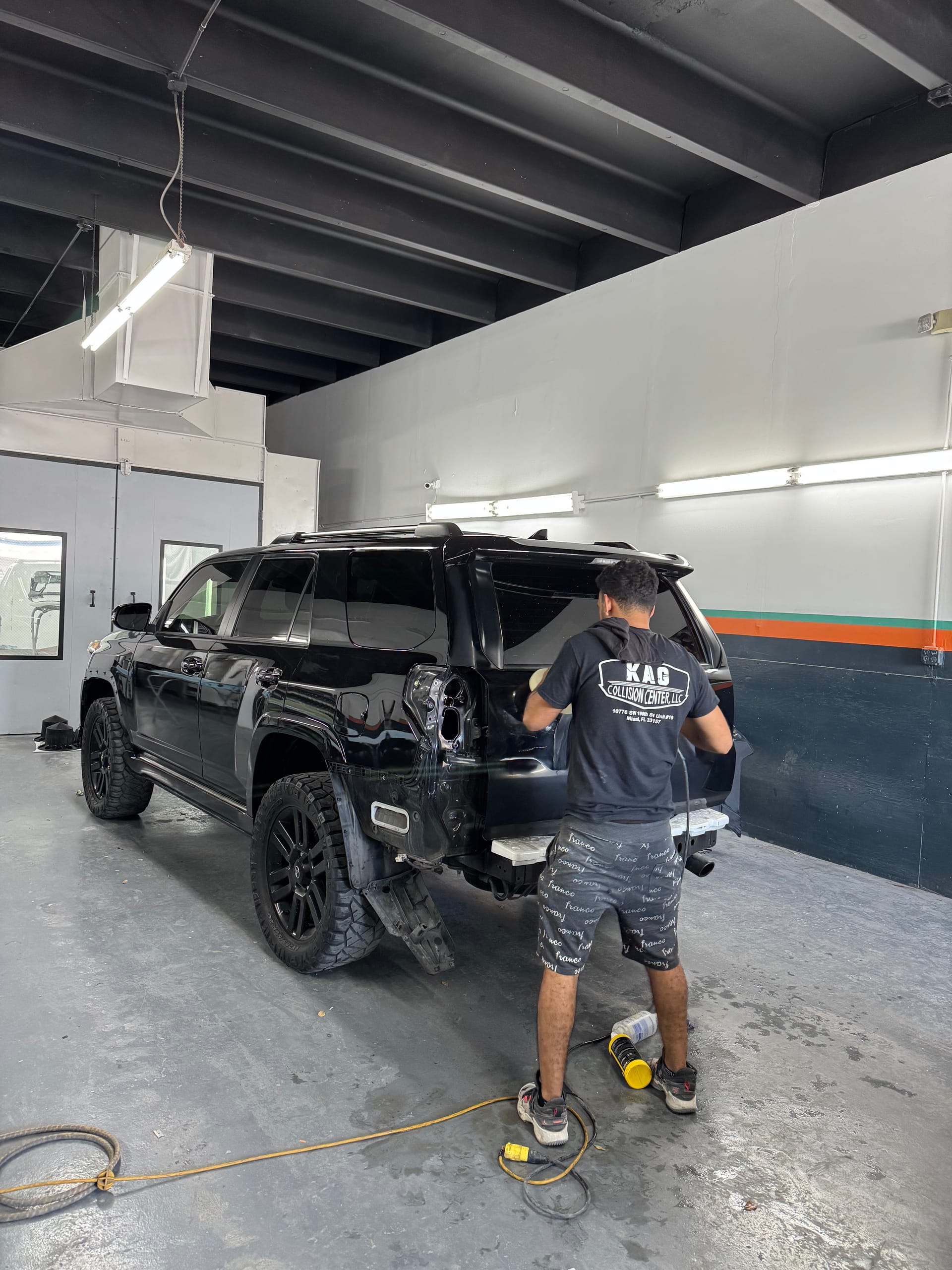 KAG technician sanding the rear quarter of a black Toyota 4Runner on the shop floor