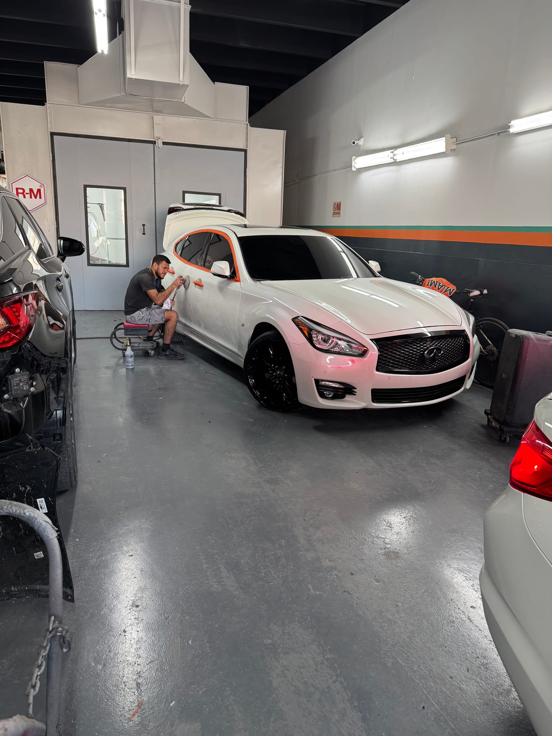 Technician sanding a white Infiniti sedan before paint